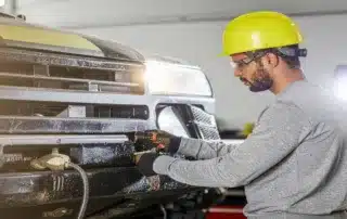 Mechanic wearing safety gear working on a vehicle's front bumper in a workshop