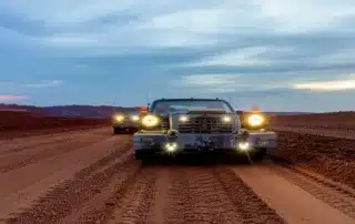 Heavy-duty off-road trucks driving on a dirt road at dusk