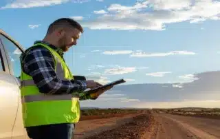 Field inspector in a high-visibility safety vest using a digital tablet next to a truck