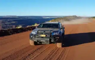Off-road vehicle driving along a dusty dirt track near an open pit mine