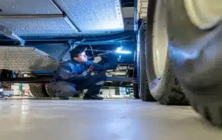 Mechanic crouching under a raised vehicle with an inspection light