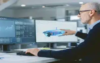 Computer setup displaying CAD software and engineering 3D designs