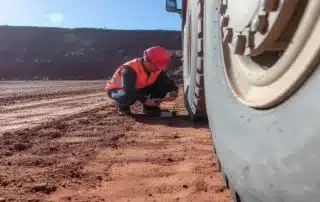 Technician inspecting the wheel end of a heavy mining vehicle on a red dirt mine site